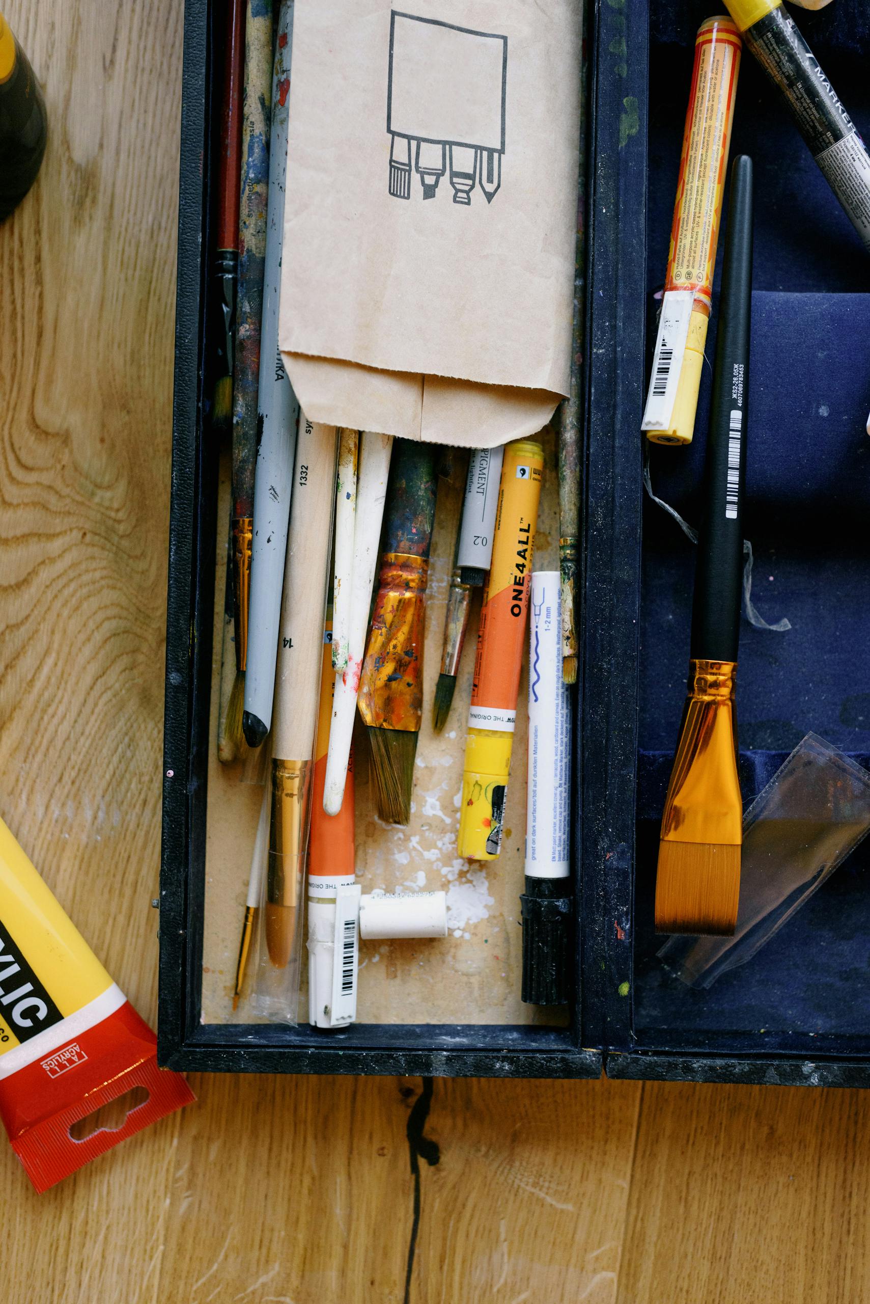 Top view of plastic case with collection of paint brushes on wooden floor in workshop